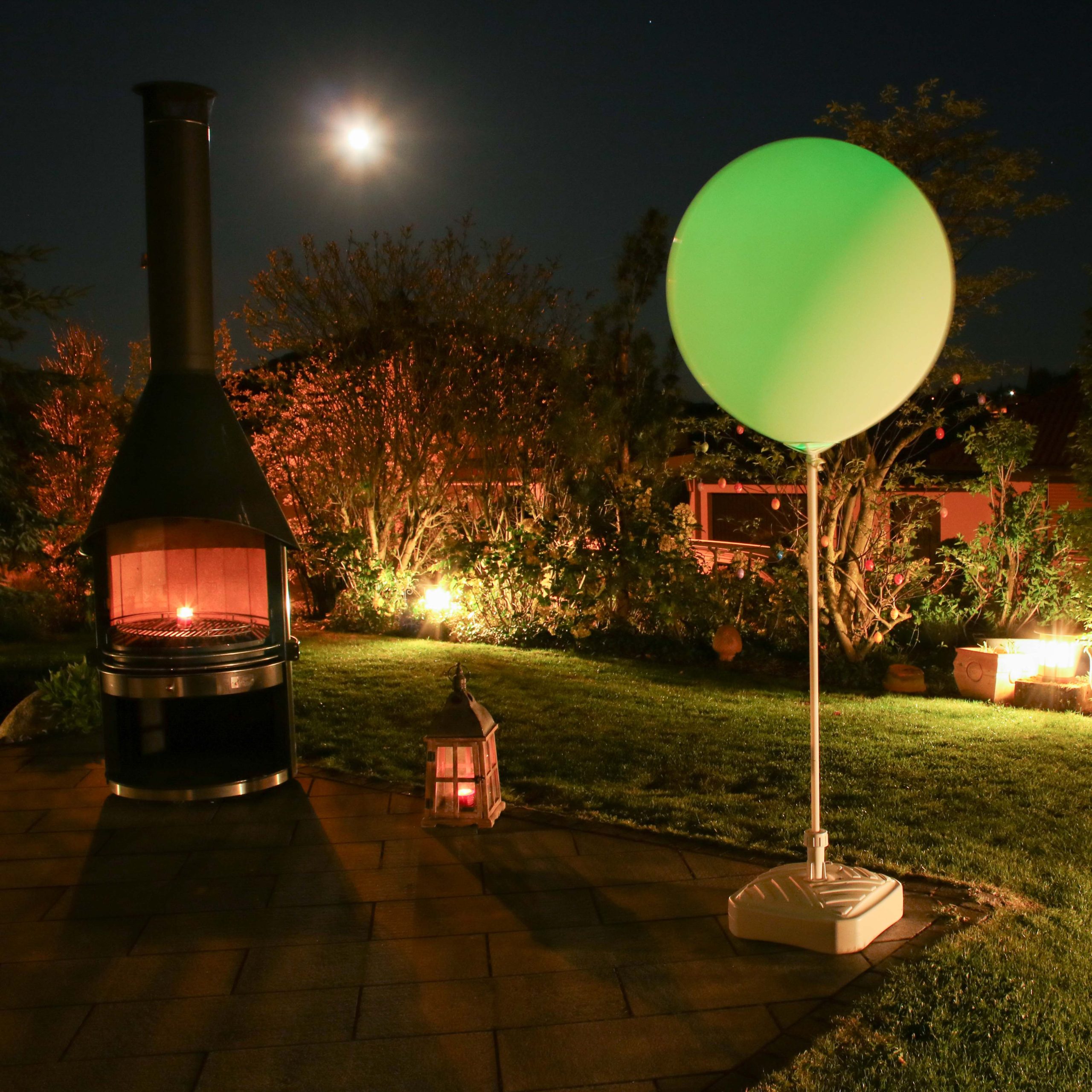 Neben einem Grill steht in einem beleuchtetem Garten ein grüner Riesenballon